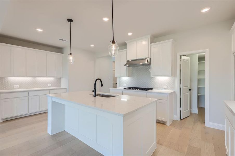 Kitchen with pendant lighting, light hardwood / wood-style floors, a kitchen island with sink, sink, and white cabinets