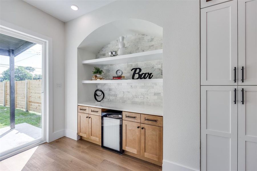 Indoor dry bar featuring light wood-style floors, tasteful backsplash, and wine cooler Indoor dry bar featuring light wood-style floors, tasteful backsplash, and wine cooler