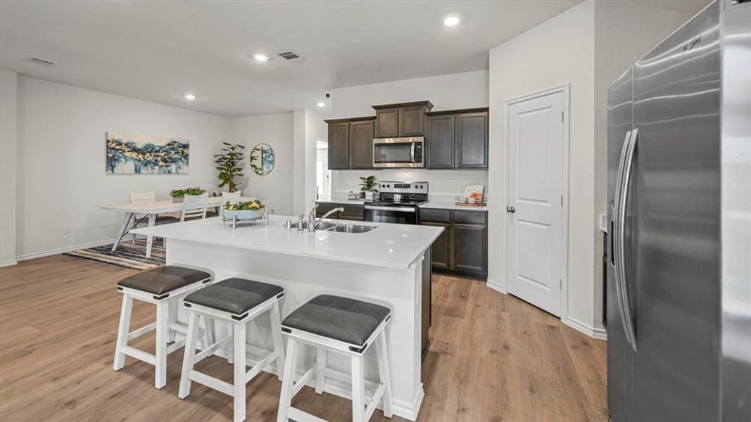Kitchen featuring stainless steel appliances, a breakfast bar, a center island with sink, recessed lighting, and light wood-style flooring