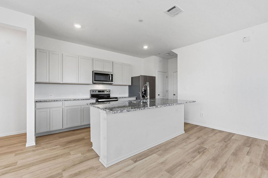 Kitchen featuring an expansive island with a breakfast bar, stainless steel appliances, light gray cabinetry, and stone countertops Kitchen featuring an expansive island with a breakfast bar, stainless steel appliances, light gray cabinetry, and stone countertops