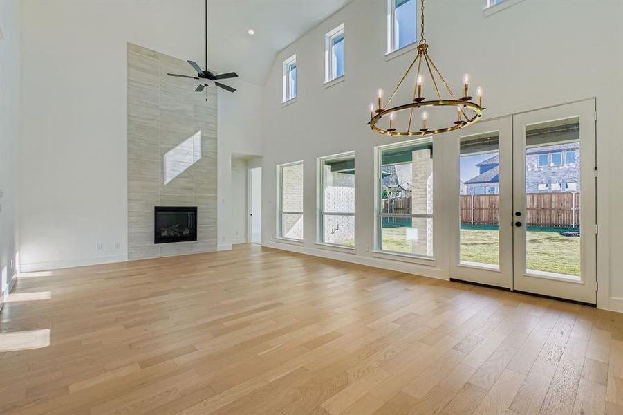Unfurnished living room with light wood finished floors, ceiling fan, a fireplace, a towering ceiling, and a chandelier
