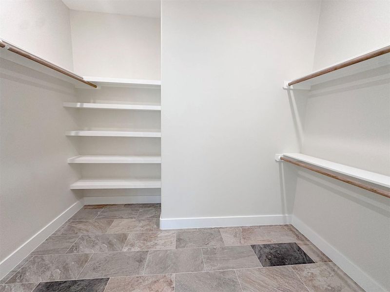 Walk in closet featuring excellent hanging rod spacew and. storage shelves, stone finish flooring