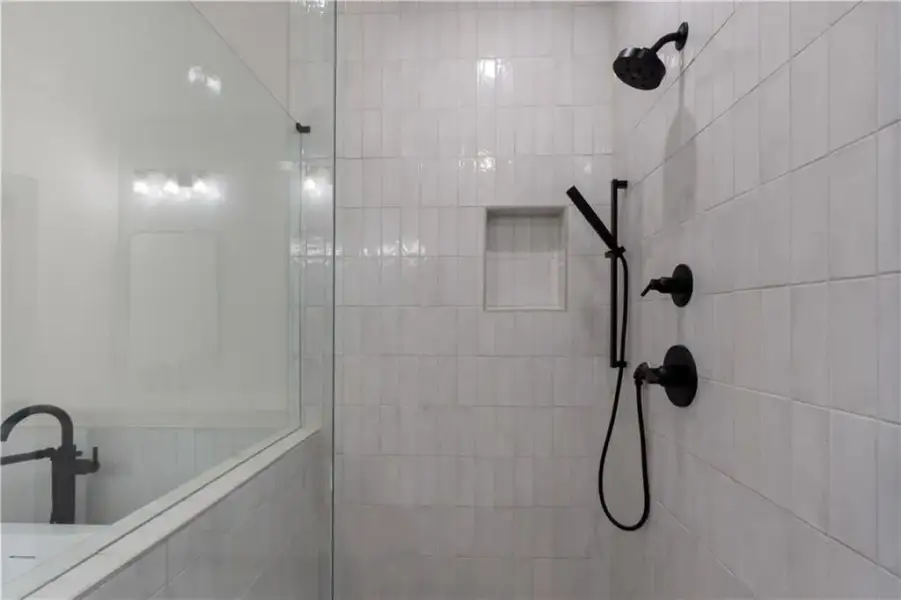 Shower enclosure featuring light-toned vertical tile, a built-in shower niche, matte black shower fixtures, a handheld showerhead, and a clear glass partition