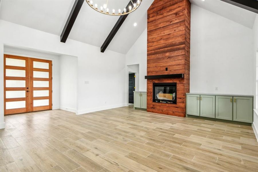 Unfurnished living room featuring high vaulted ceiling, a chandelier, light wood-style flooring, a fireplace, and beam ceiling Unfurnished living room featuring high vaulted ceiling, a chandelier, light wood-style flooring, a fireplace, and beam ceiling