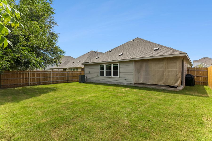 Expansive green lawn surrounds the property, featuring a durable wood privacy fence and a mature shade tree