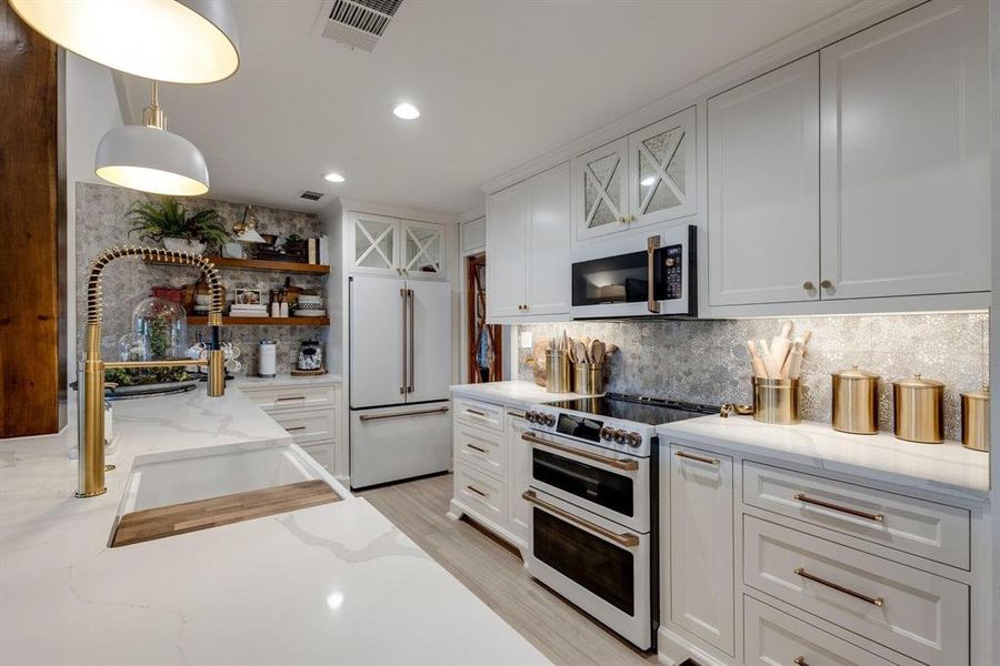Kitchen with high end appliances, sink, light stone countertops, decorative light fixtures, and white cabinetry