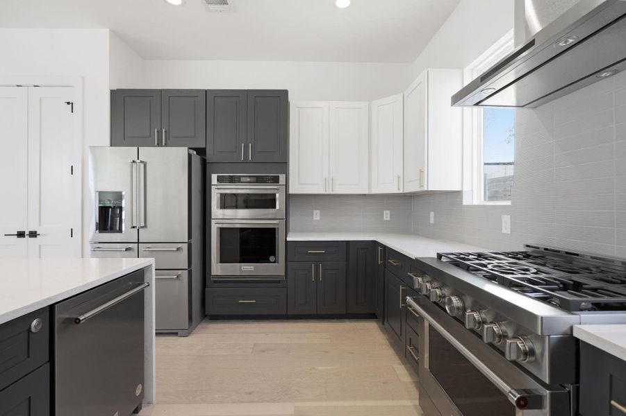 Kitchen with dual tone cabinetry, premium appliances, extractor fan, light stone countertops, and light wood-style flooring