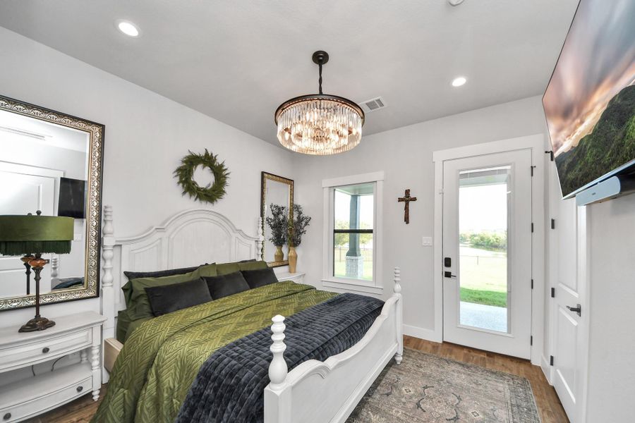 Charming bedroom with elegant chandelier lighting, featuring a cozy bed framed by stylish decor and a large window leading to serene outdoor views.