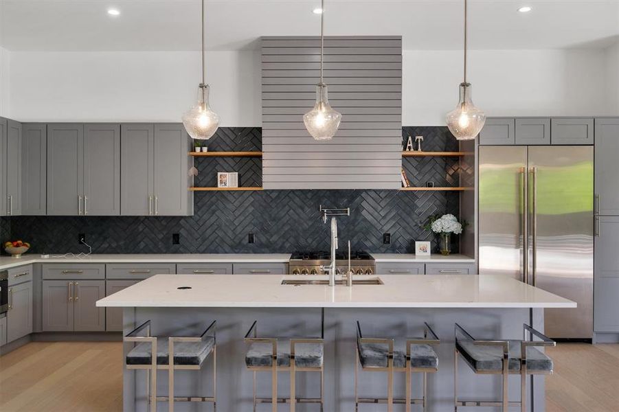 Kitchen featuring gray cabinets, light hardwood / wood-style floors, a center island with sink, and built in fridge