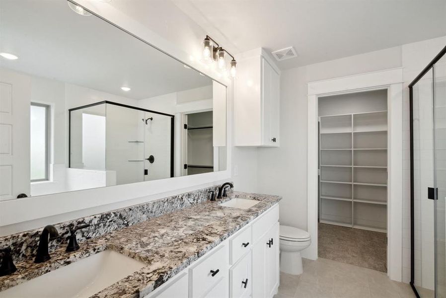 Bathroom featuring toilet, tile patterned floors, a shower with door, and double sink vanity