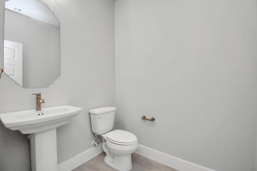 This half bathroom features a stylish pedestal sink, modern hardware, and bright recessed lighting, creating a sleek and inviting space. Sample photo of completed home with similar floor plan. Actual colors and selections may vary.