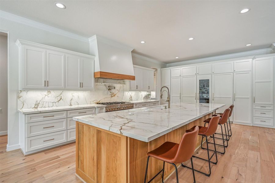 The showstopper kitchen boasts an oversized island with generous seating, gorgeous Calacatta Macchia Vecchia porcelain countertops and contrasting natural wood cabinetry, complemented by crisp white perimeter cabinetry & warm brass-tone hardware.