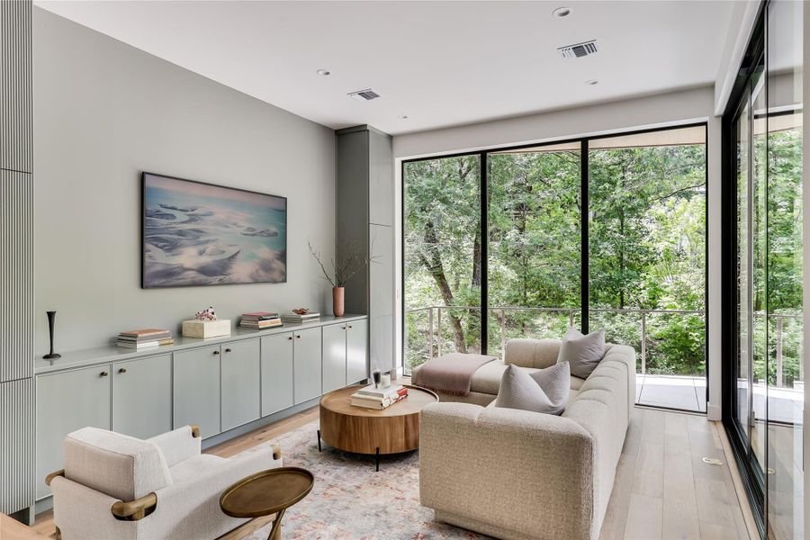 Spacious living area featuring floor-to-ceiling windows, built-in cabinetry, recessed lighting, wood-finish flooring, and a sliding glass door opening to a balcony
