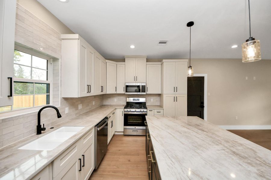 Modern kitchen featuring quartz countertops, a large center island, stainless steel appliances, custom cabinetry, and a farmhouse-style sink, all accented by stylish pendant lighting and abundant natural light.