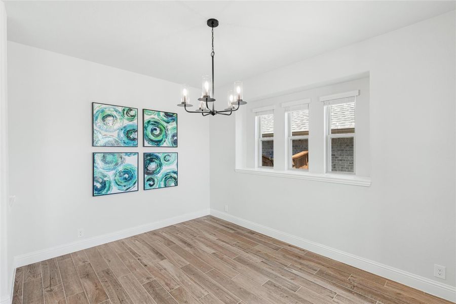 Empty dining room with hardwood floors, black chandelier, and four teal wall art panels Empty dining room with hardwood floors, black chandelier, and four teal wall art panels