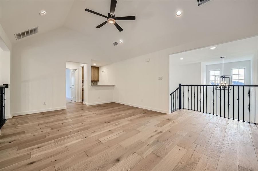 Unfurnished living room featuring light hardwood / wood-style floors, high vaulted ceiling, and ceiling fan with notable chandelier