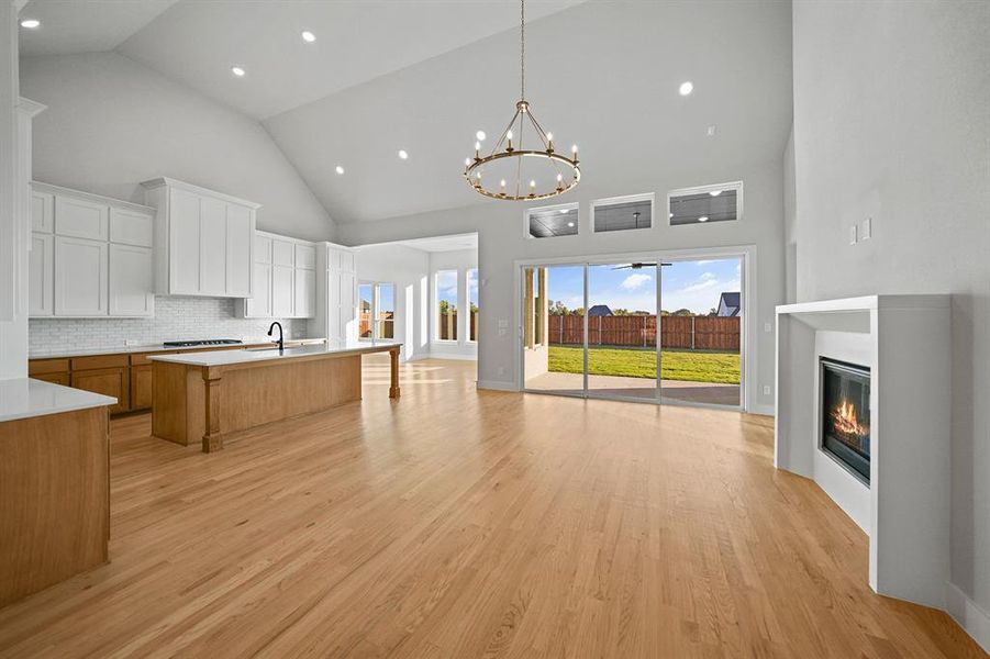 Kitchen featuring high vaulted ceiling, a kitchen breakfast bar, brown cabinetry, a glass covered fireplace, and open floor plan Kitchen featuring high vaulted ceiling, a kitchen breakfast bar, brown cabinetry, a glass covered fireplace, and open floor plan