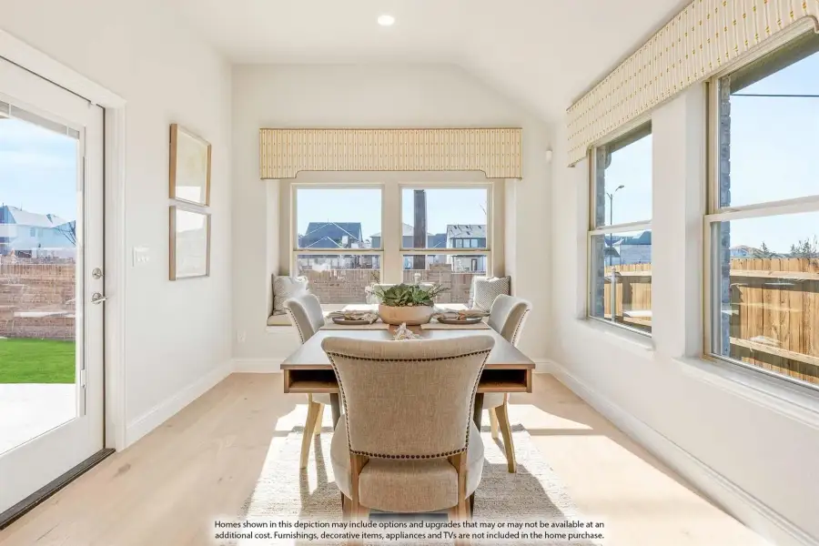 Bright dining nook with vaulted ceiling, wood table, upholstered chairs, and large windows with patio door access.