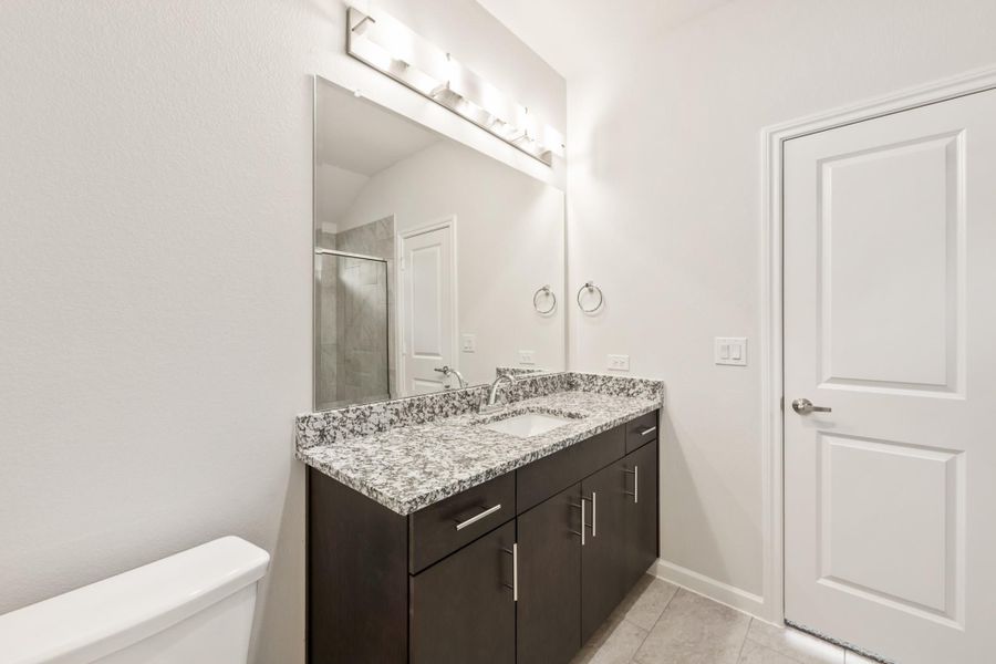 Bathroom with dark wood double vanity, granite countertop, large mirror, and walk-in shower visible in reflection Bathroom with dark wood double vanity, granite countertop, large mirror, and walk-in shower visible in reflection