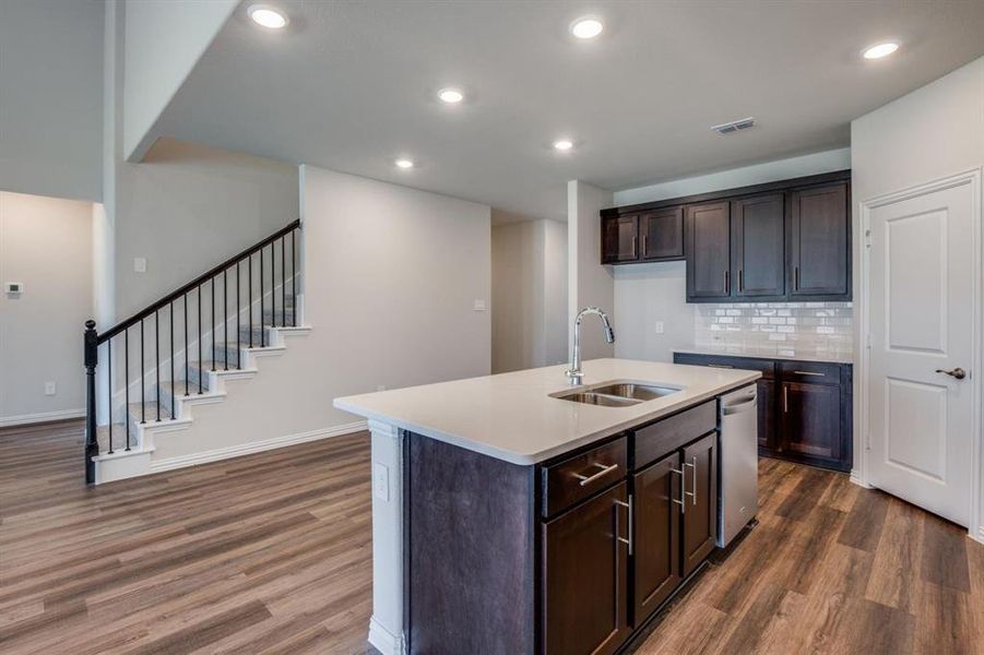 Kitchen with dark hardwood / wood-style flooring, decorative backsplash, sink, dishwasher, and a kitchen island with sink