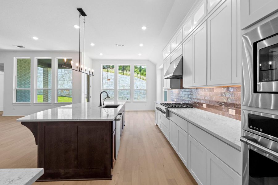 Kitchen featuring backsplash, light wood-style flooring, a kitchen island with sink, light stone counters, and recessed lighting