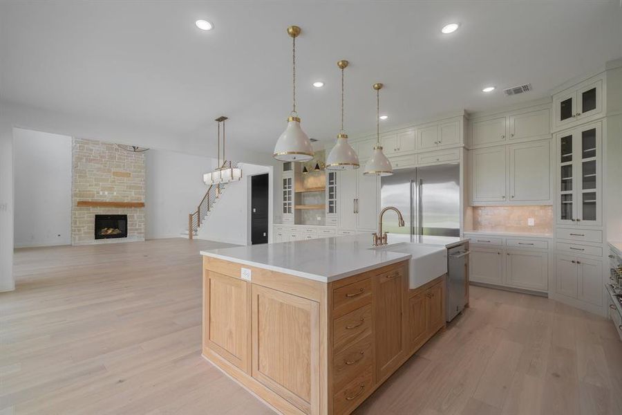 Kitchen with a fireplace, stainless steel appliances, light wood-type flooring, sink, and a center island with sink