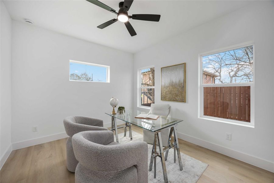 A bright, minimalist, first floor office space features a glass desk, plush modern chairs, and large windows that fill the room with natural light.