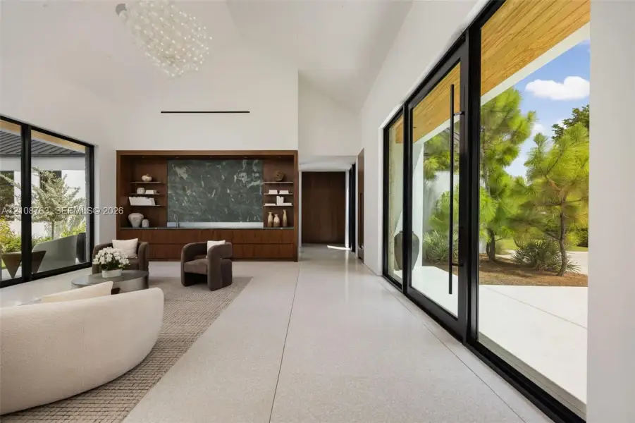 Vaulted ceilings, large-format tile flooring, built-in floor-to-ceiling wooden cabinetry with integrated stone-surround shelving, and expansive floor-to-ceiling black-framed glass sliding doors