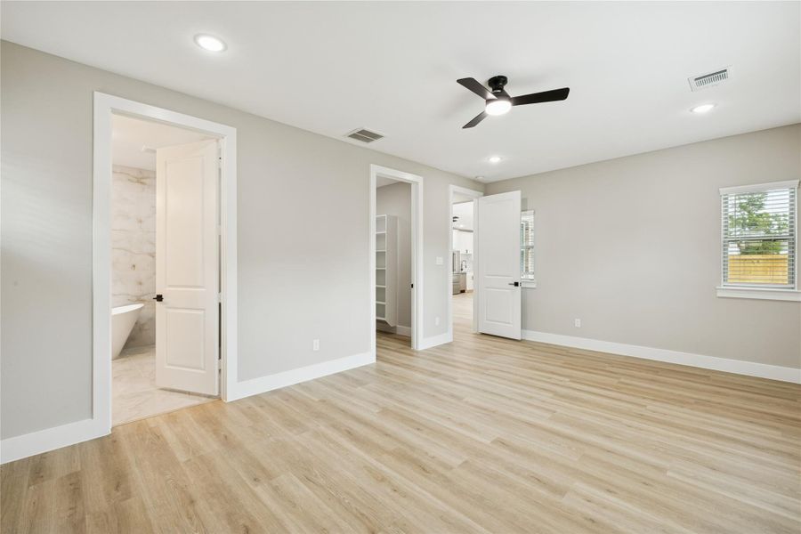 Spacious primary bedroom with sleek wood flooring, modern ceiling fan, and direct access to a luxurious ensuite bathroom.