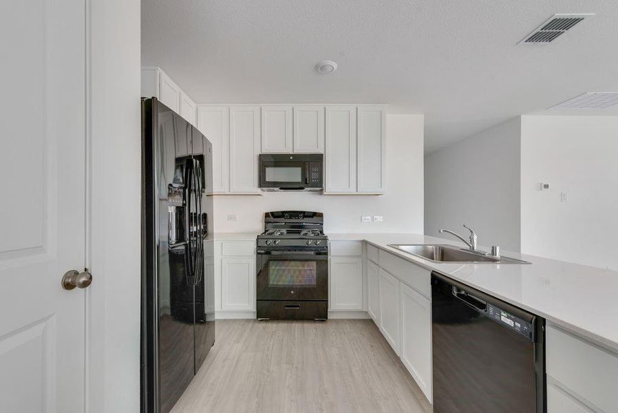 Kitchen featuring black appliances, light wood-style flooring, white cabinets, and a peninsula