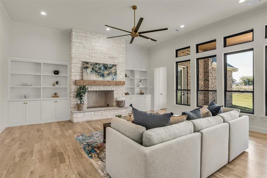 Living room with recessed lighting, ceiling fan, a stone fireplace, light wood finished floors, and crown molding