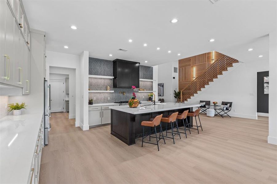 Kitchen with a kitchen breakfast bar, white cabinetry, backsplash, open shelves, and an island with sink