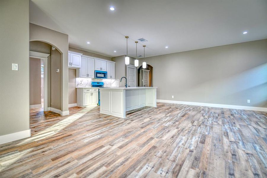 Kitchen with arched walkways, recessed lighting, hanging light fixtures, a kitchen island with sink, and white cabinets