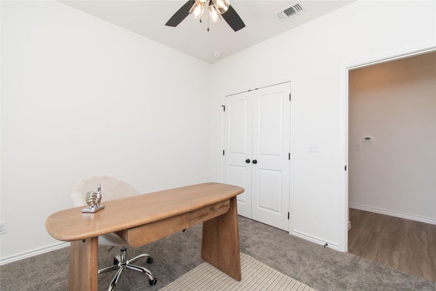 Carpeted office space featuring ceiling fan and baseboards