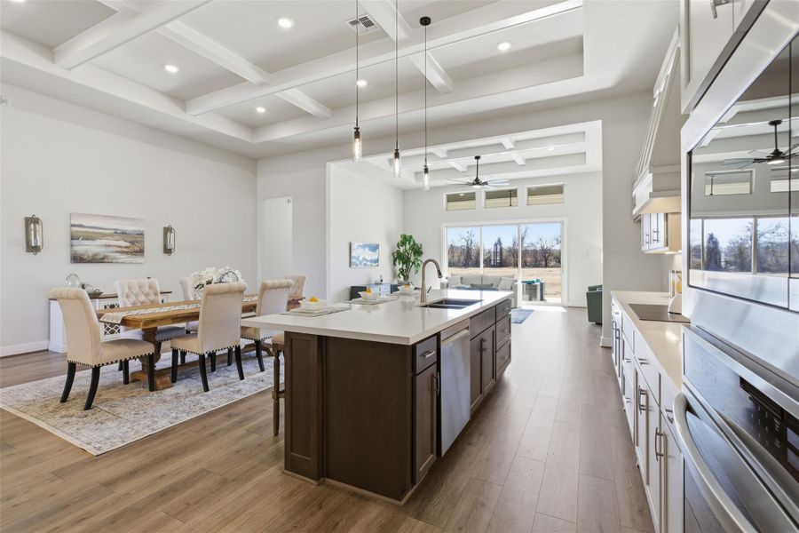 Dual tone kitchen with coffered ceiling, a ceiling fan, a kitchen island with sink, open floor plan, and hanging light fixtures