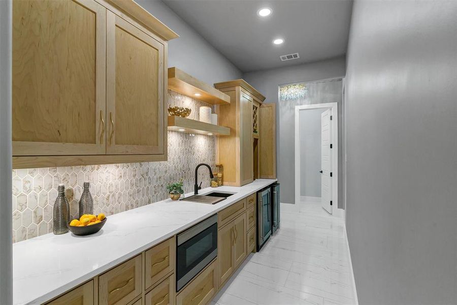 Kitchen featuring tasteful backsplash, sink, light stone countertops, stainless steel microwave, and light brown cabinets