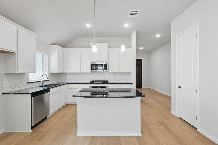 Kitchen with a kitchen island, dark stone counters, appliances with stainless steel finishes, white cabinetry, and recessed lighting Kitchen with a kitchen island, dark stone counters, appliances with stainless steel finishes, white cabinetry, and recessed lighting