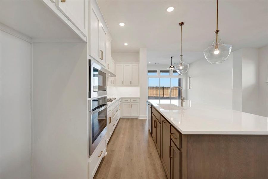 Kitchen featuring dual tone cabinets, hanging light fixtures, an island with sink, light wood-style floors, and stainless steel appliances Kitchen featuring dual tone cabinets, hanging light fixtures, an island with sink, light wood-style floors, and stainless steel appliances