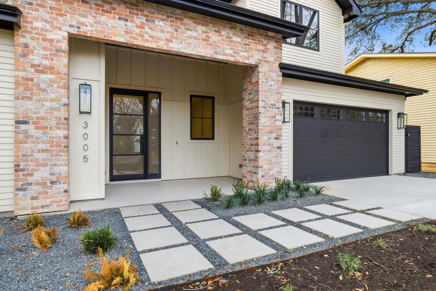 View of exterior entry with covered porch, concrete driveway, a garage, board and batten siding, and brick siding