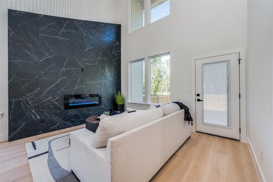 Living room with a high end fireplace, a towering ceiling, light hardwood / wood-style floors, and tile walls