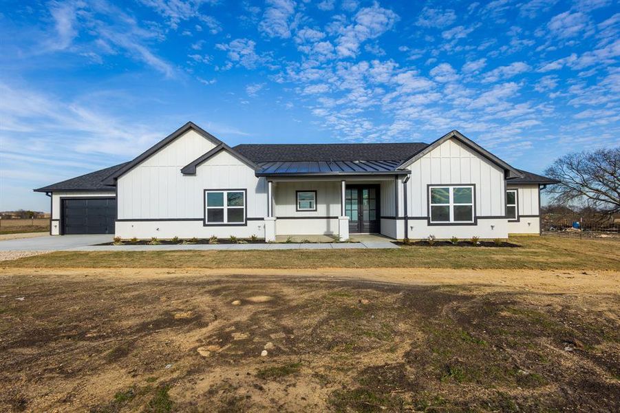 Modern farmhouse with covered porch, a garage, and a front lawn