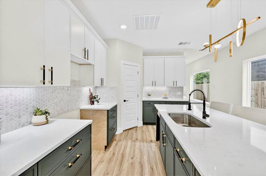 Kitchen featuring a large island with an undermount sink, white upper cabinetry, dark lower cabinetry, white countertops, and wood-finish flooring