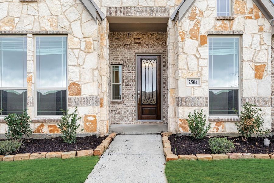Home entrance with stone and brick exterior, dark wood front door with glass panel, and landscaped walkway