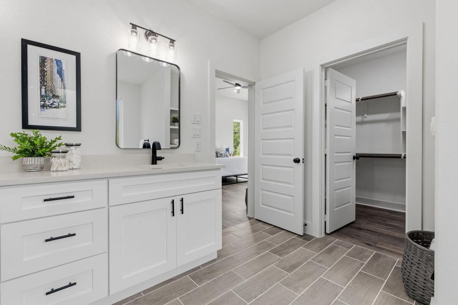 A well-appointed primary bathroom featuring sleek cabinetry, modern fixtures, and direct access to a spacious walk-in closet.