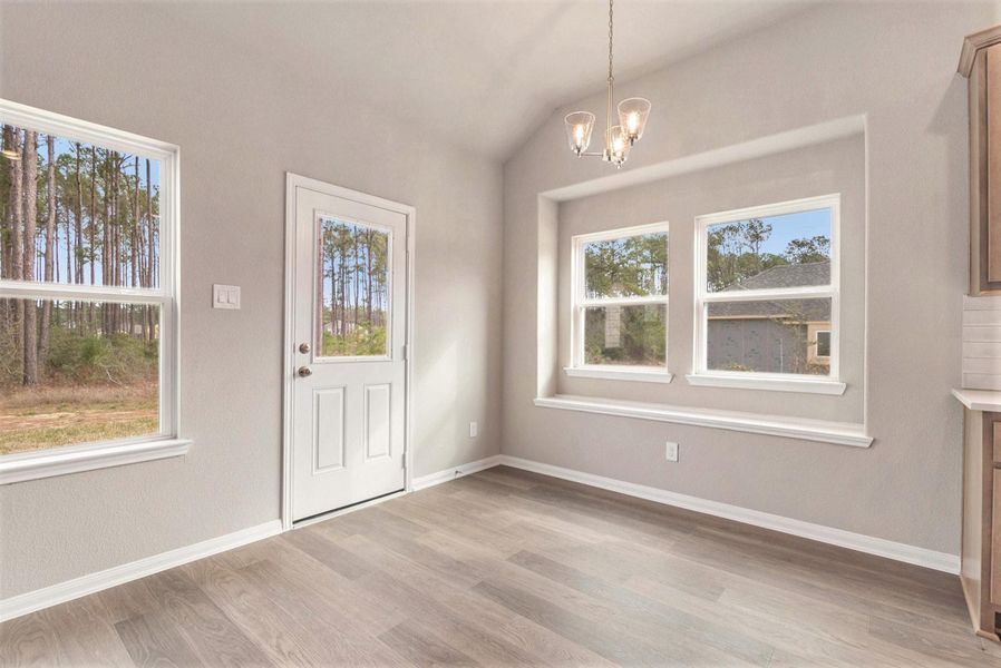 Bright room with large windows and a glass door, offering scenic views of trees. It features light wood flooring, neutral walls, and a modern chandelier, providing a welcoming entry or dining space.
