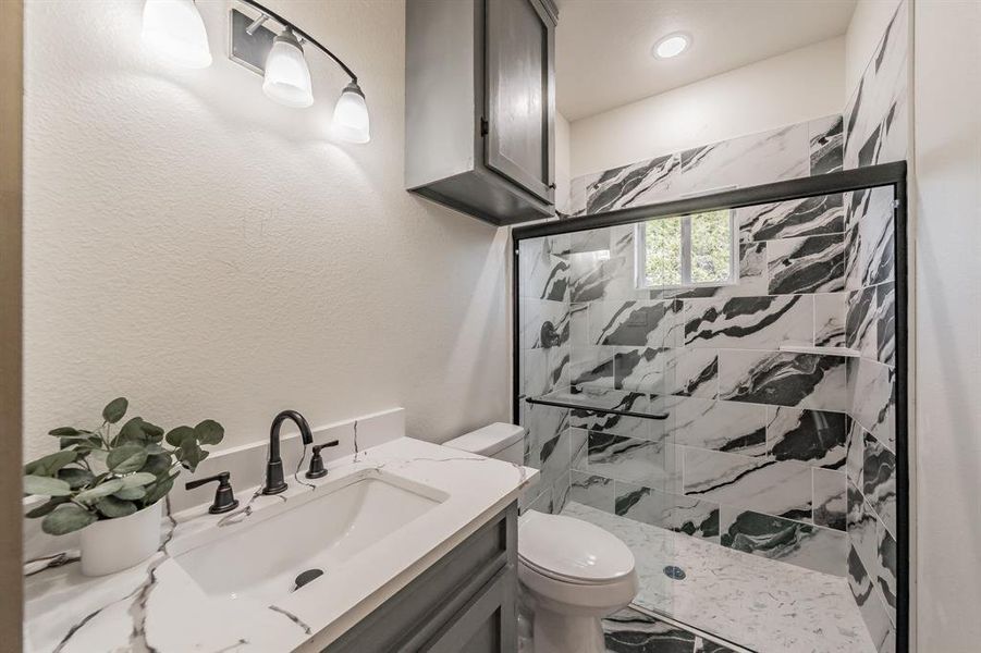Bathroom with a marble finish shower, vanity, and a textured wall