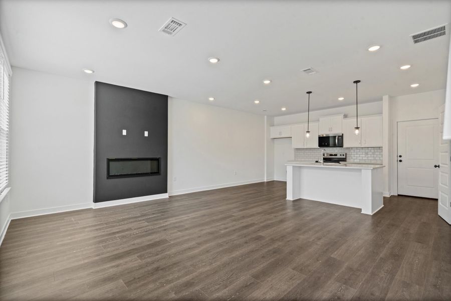 Open-concept living area with wood-finish flooring, recessed lighting, and a linear fireplace Open-concept living area with wood-finish flooring, recessed lighting, and a linear fireplace