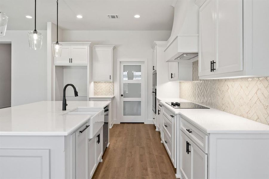 Kitchen featuring tasteful backsplash, an island with sink, white cabinets, decorative light fixtures, and dark wood finished floors