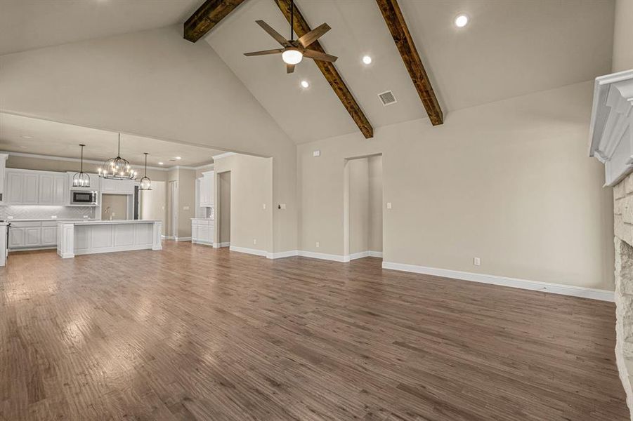 Unfurnished living room with high vaulted ceiling, ceiling fan with notable chandelier, hardwood / wood-style floors, and beam ceiling