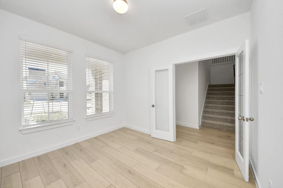 Experience the perfect blend of sophistication and warmth in this home office, boasting elegant wood-look tile flooring and flooded with natural light from expansive windows and French doors. Sample photo of completed home with similar floor plan. Actual colors and selections may vary.